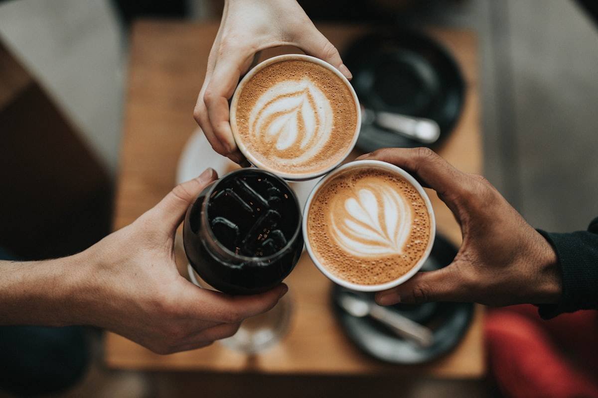 Three friends raising cups of latte over a table